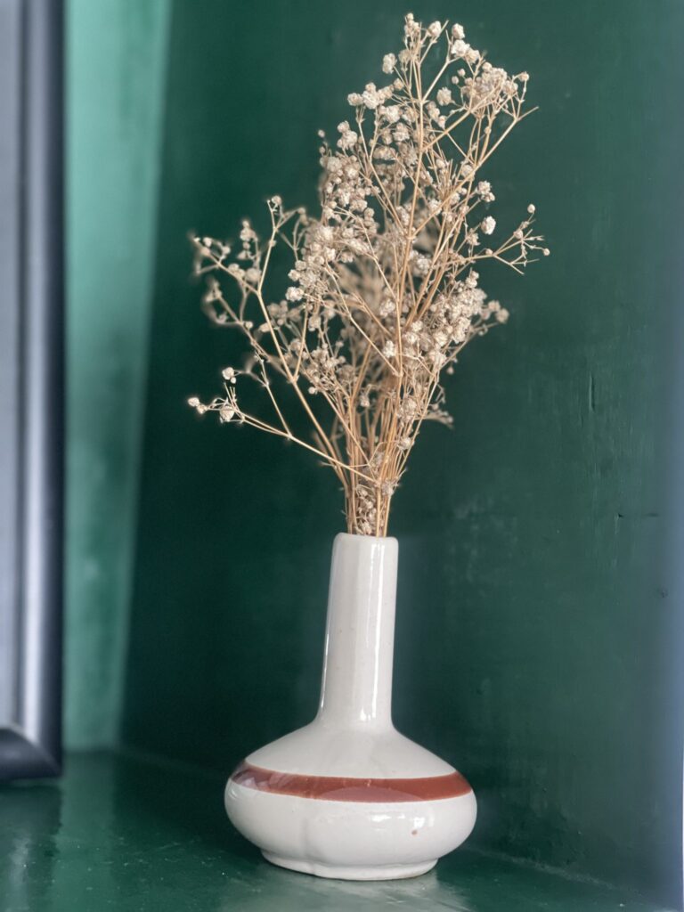 Jarrón de cerámica blanca con flores secas sobre fondo verde