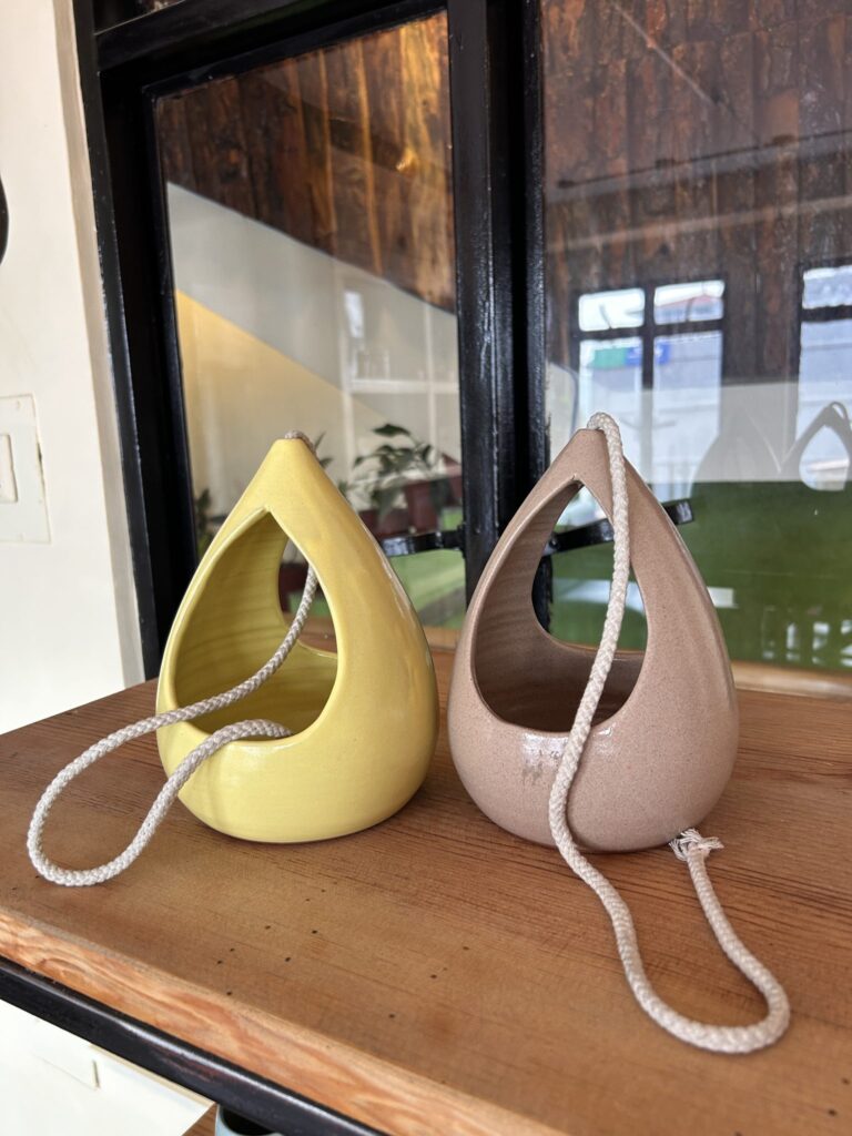 Dos maceteros de cerámica en forma de gota, amarillo y rosa, sobre una balda