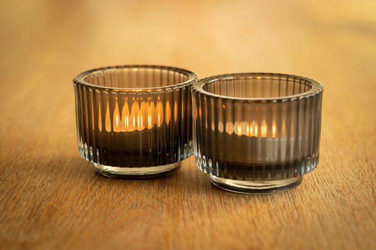 Dos velas encendidas en vasos de cristal sobre una mesa de madera